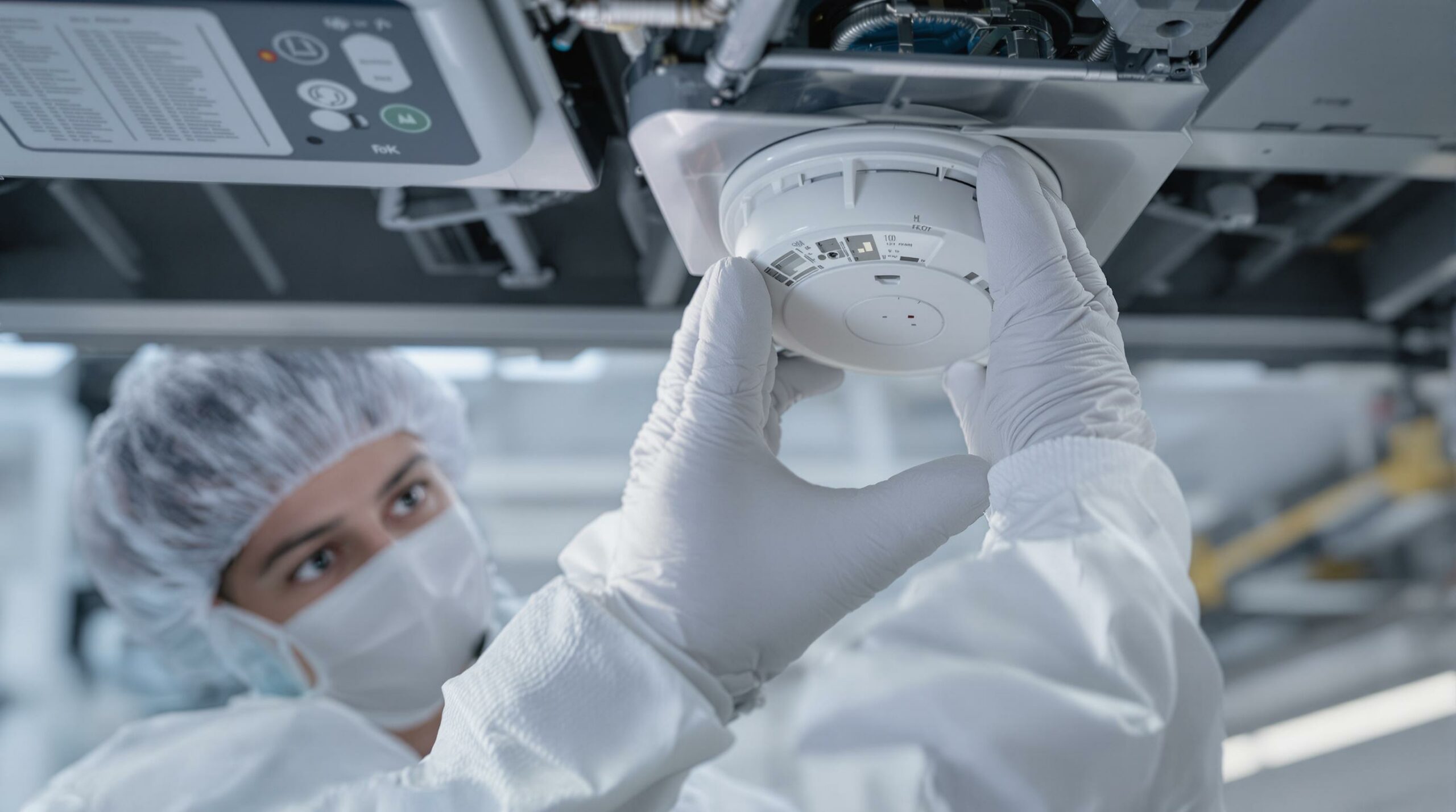 Technician installing a smoke detector in a cleanroom.